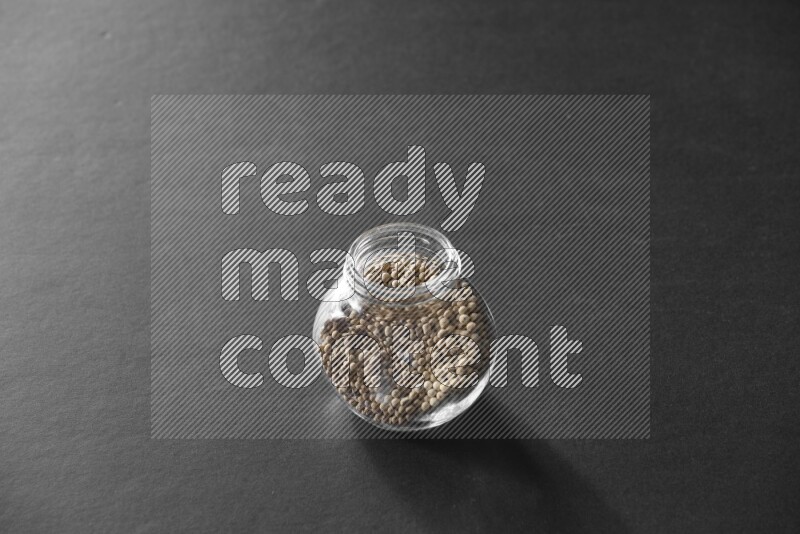 A glass spice jar full of white peppers on black flooring