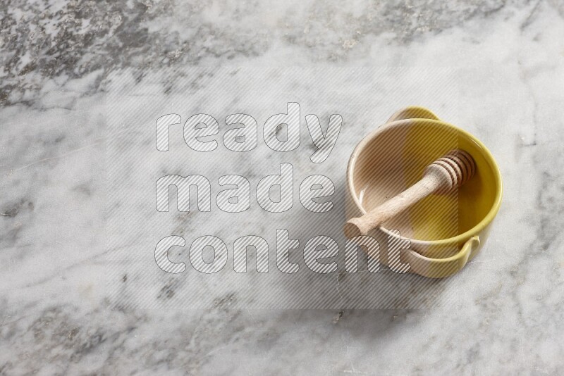 Multicolored pottery bowl with wooden honey dipper in it on grey marble background