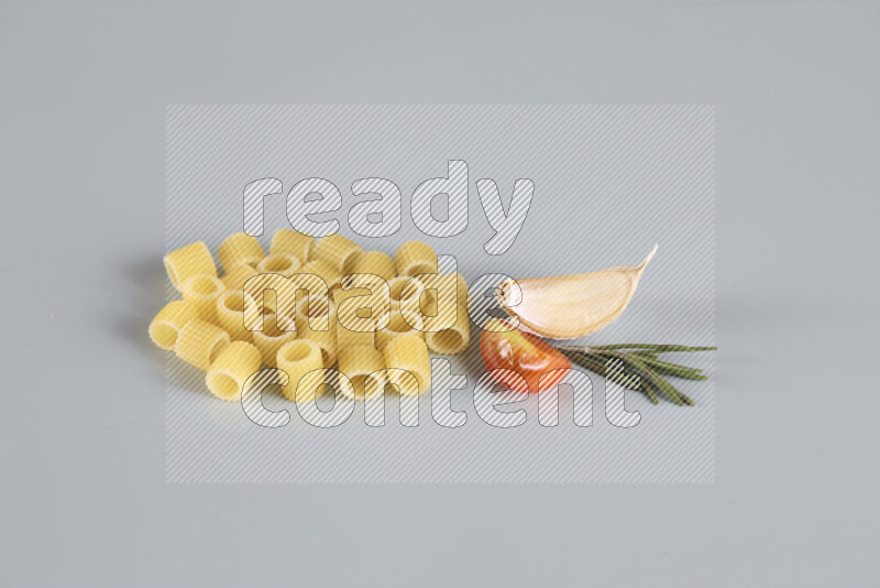 Raw pasta with different ingredients such as cherry tomatoes, garlic, onions, red chilis, black pepper, white pepper, bay laurel leaves, rosemary, cardamom and mushrooms on light blue background