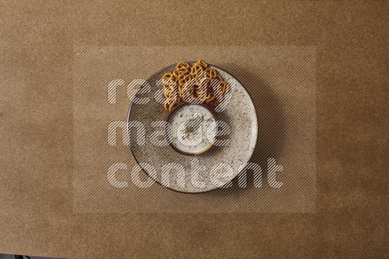 Assorted snacks on a pottery plate with a dipping on brown background