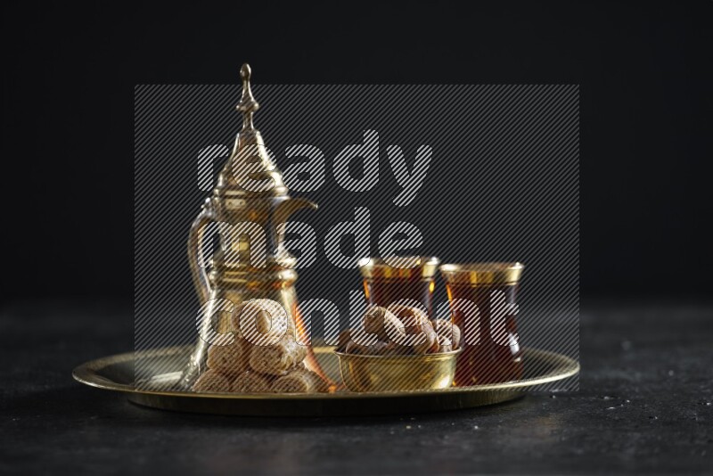 Oriental sweets with dates and a drink on a metal tray in a dark setup
