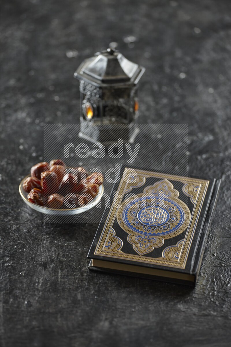A silver lantern with different drinks, dates, nuts, prayer beads and quran on textured black background