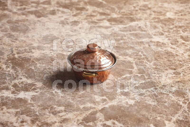 A small copper pot on beige marble background