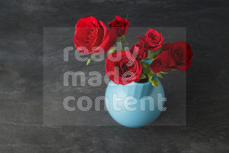 An arrangement of vivid red roses in a blue vase on black marble background