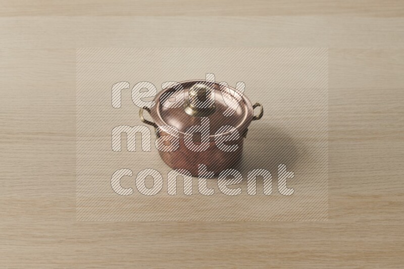 A small copper pot on light wooden background