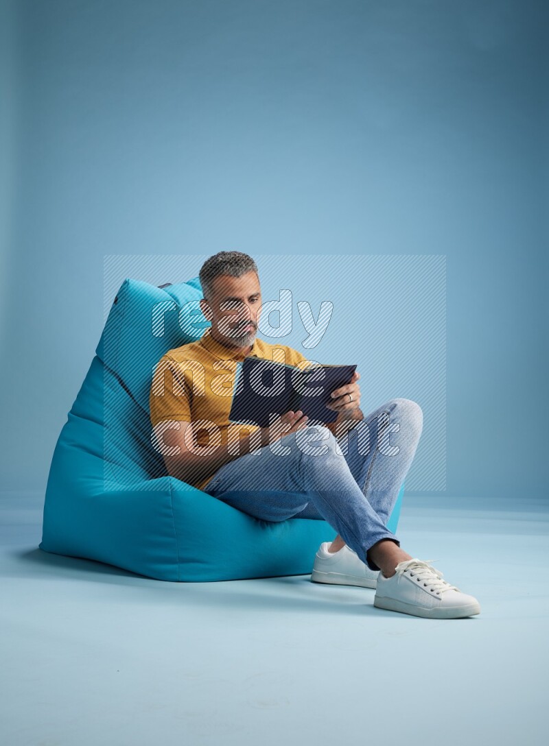 A man sitting on a blue beanbag and reading a book