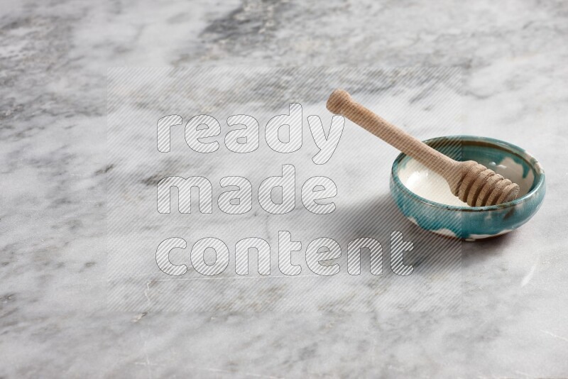 Multicolored pottery bowl with wooden honey dipper in it on grey marble background