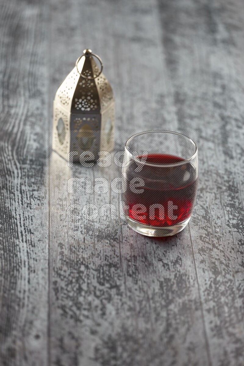 A silver lantern with different drinks, dates, nuts, prayer beads and quran on grey wooden background