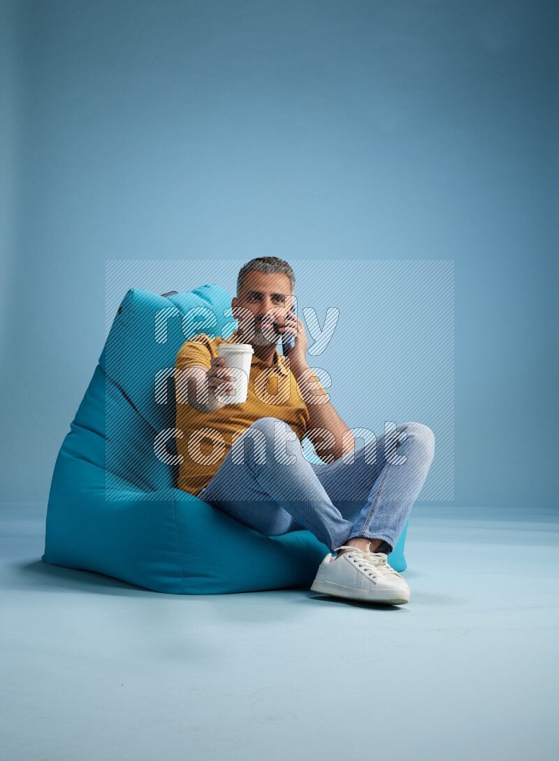 A man sitting on a blue beanbag and drinking coffee
