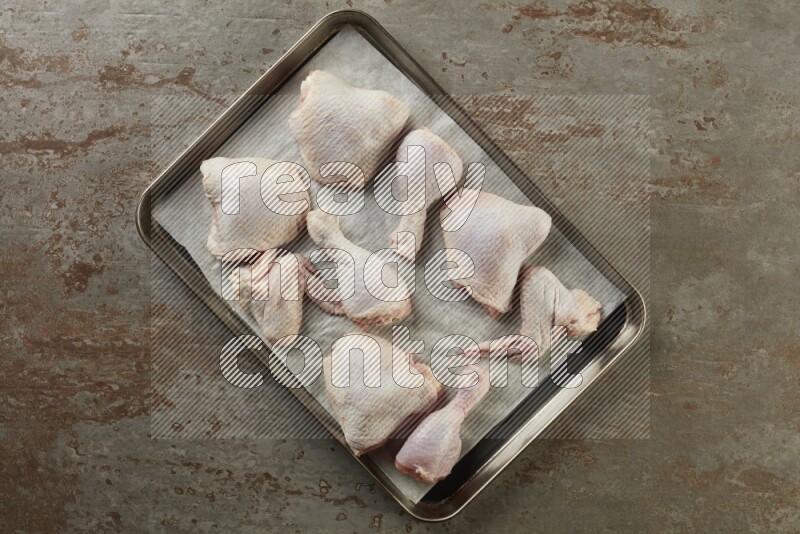 Mixed fresh chicken pieces in an oven tray on a textured rustic background