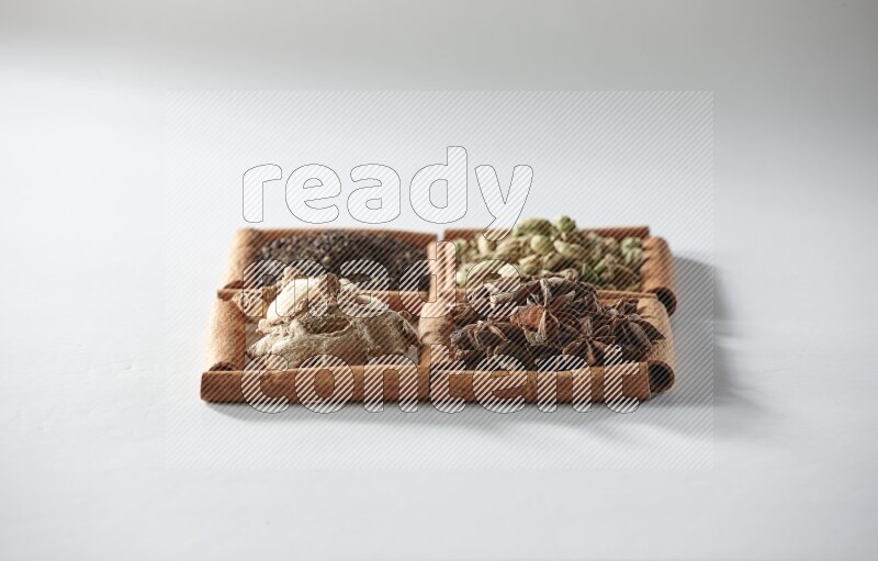 4 مربعات من أعواد القرفة ممتلئة بالشاي والهيل واليانسون والزنجبيل على أرضية بيضاء