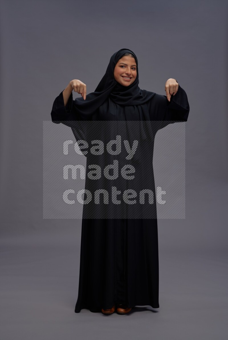 Saudi woman wearing Abaya standing interacting with the camera on gray background