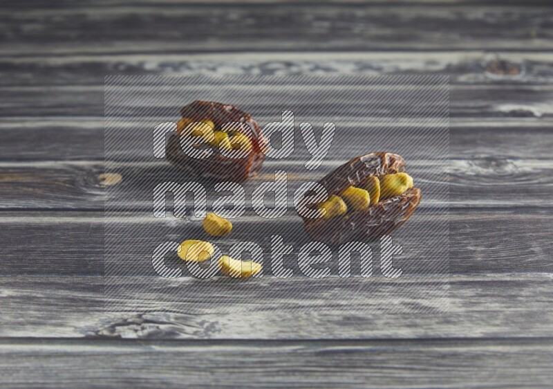 two pistachio stuffed madjoul dates on a wooden grey background