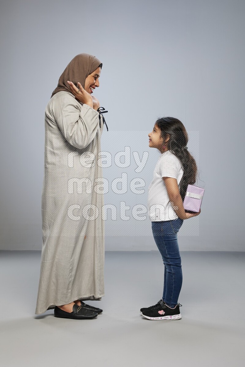A girl standing hiding a gift behind her back for her mother on gray background