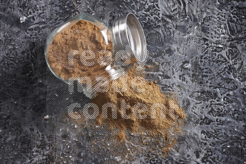 Flipped herbal glass jar full of cinnamon powder on textured black background