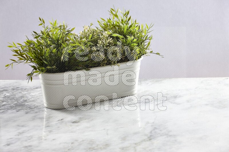 Multiple green artificial plants in white pot on grey marble background