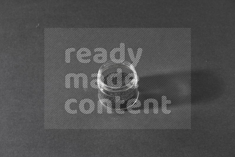 A glass jar full of black seeds on a black flooring