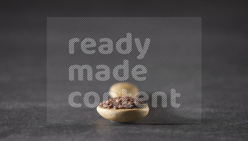 A wooden spoon full of flaxseeds on a black flooring