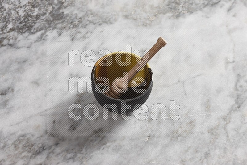 Multicolored pottery bowl with wooden honey dipper in it on grey marble background