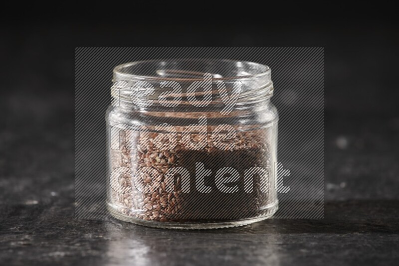 A glass jar full of flaxseeds on a textured black flooring