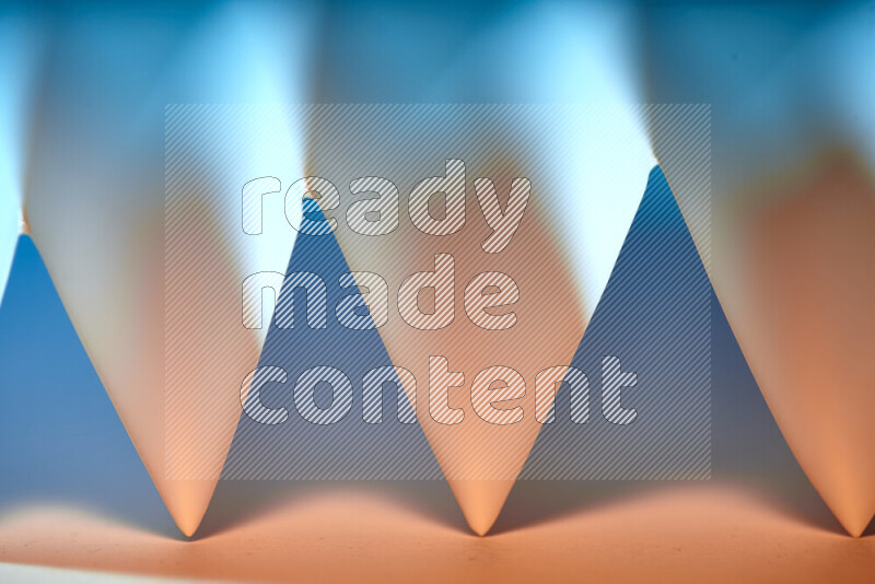 A close-up abstract image showing sharp geometric paper folds in blue gradients and warm tones