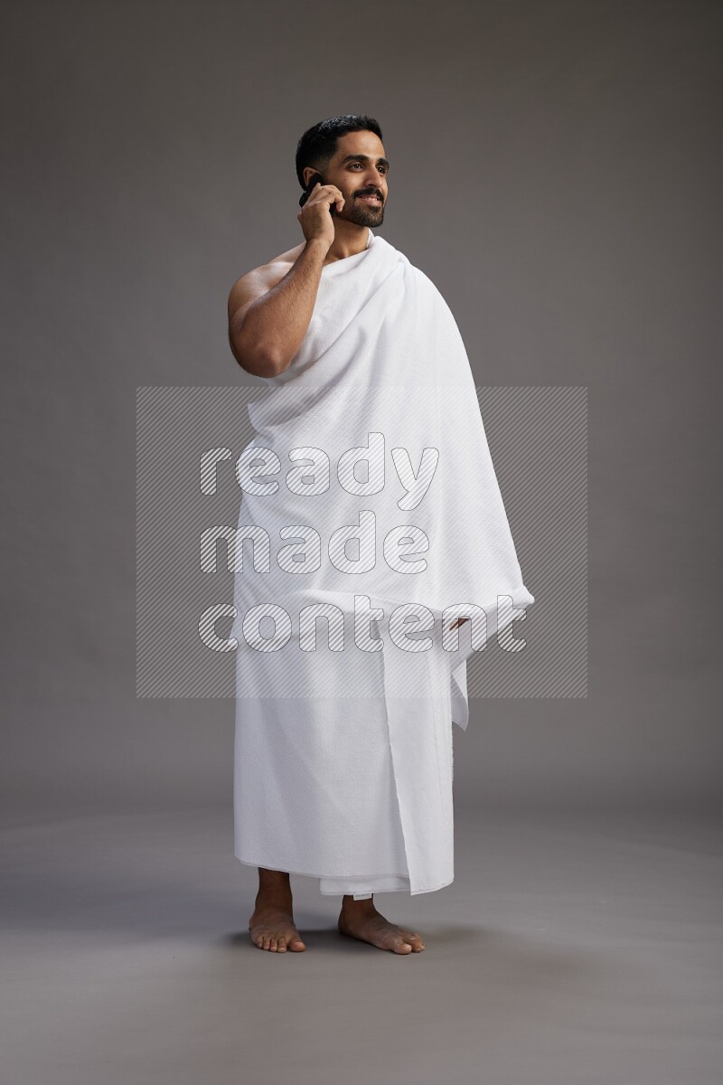 A man wearing Ehram Standing talking on phone on gray background