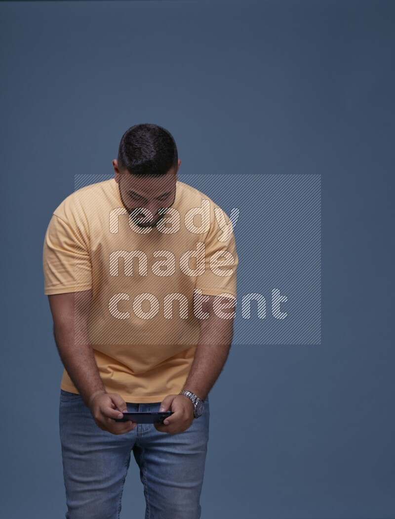 A man Playing Games on Smartphone on Blue Background wearing Orange T-shirt