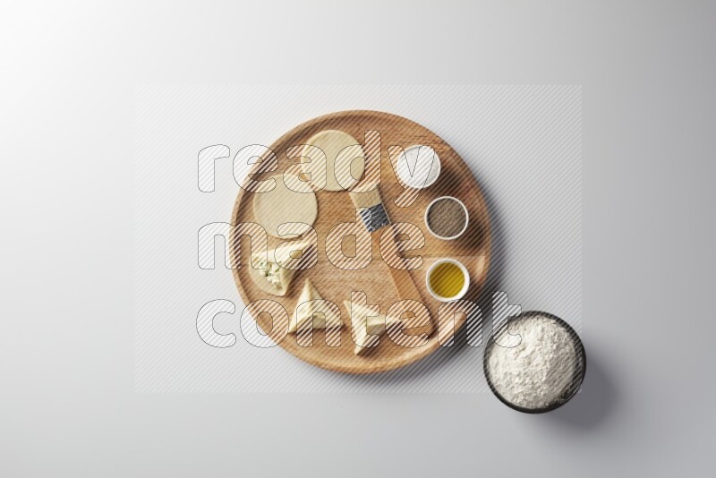 two closed sambosas and one open sambosa filled with cheese while flour, salt, black pepper and oil with oil brush aside in a wooden dish on a white background