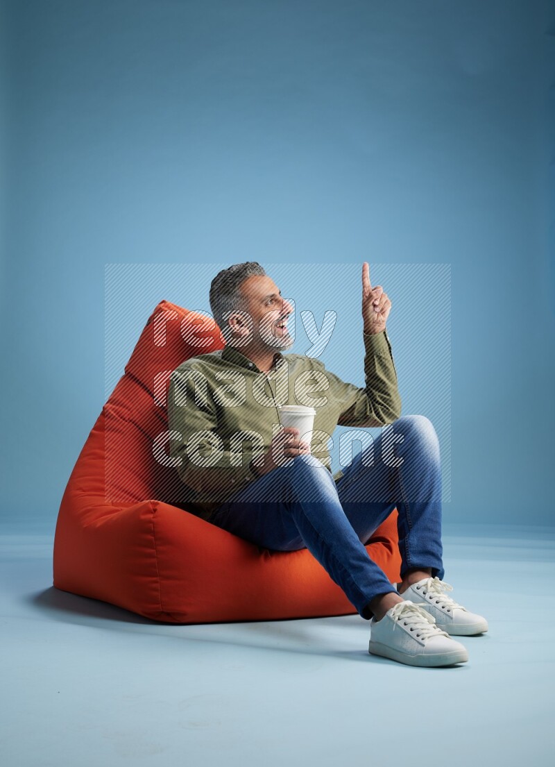 A man sitting on an orange beanbag and drinking coffee