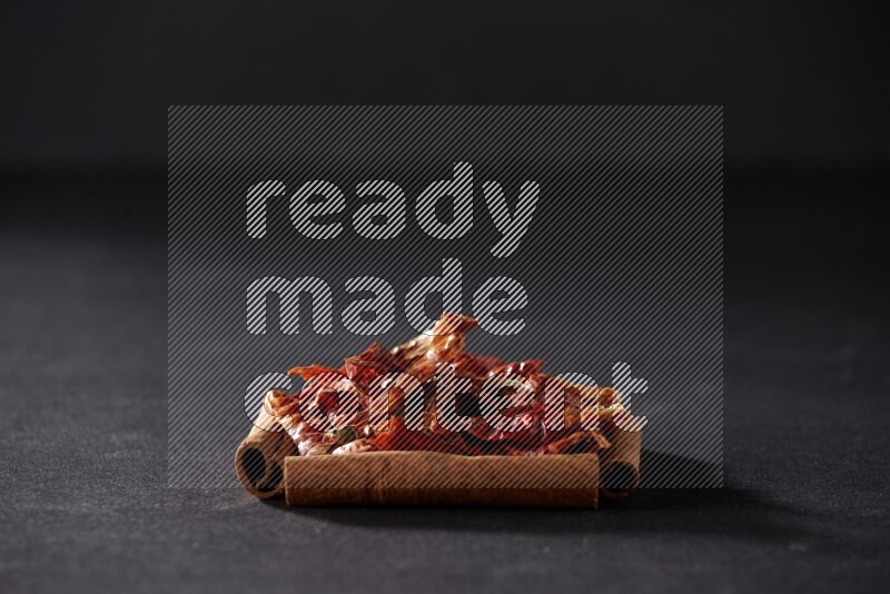 أربعة من أعواد القرفة مكونة شكل مربع بداخلها فلفل حار علي خلفية سوداء