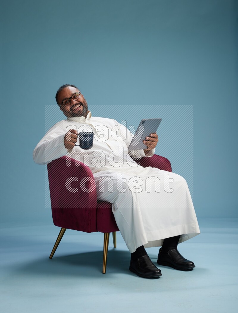 Saudi Man without shimag sitting on chair working on tablet on blue background