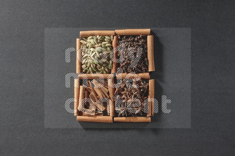 4 squares of cinnamon sticks full of cinnamon, cardamom, cloves and star anise on black flooring