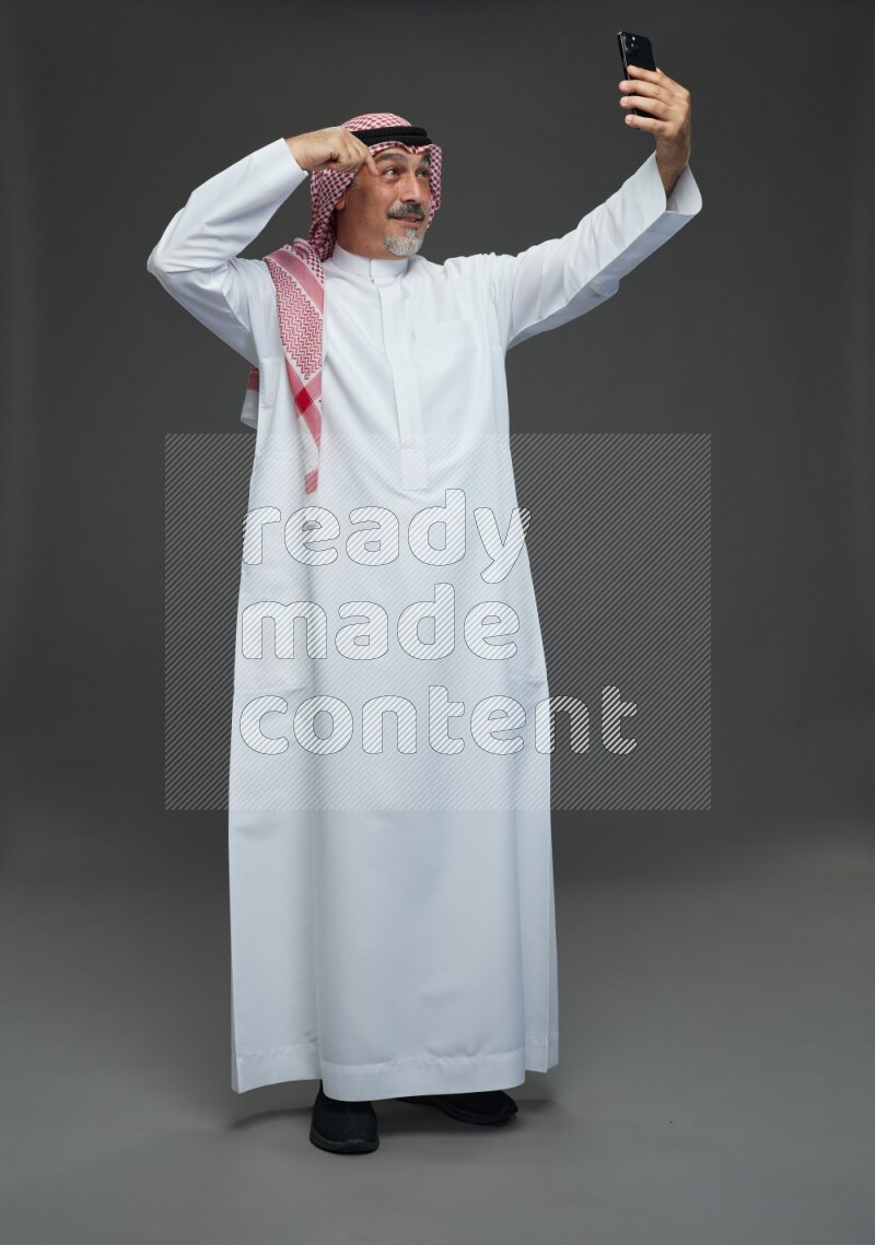 Saudi man with shomag Standing taking selfie on gray background