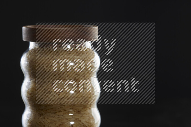 Basmati golden rice in a glass jar on black background