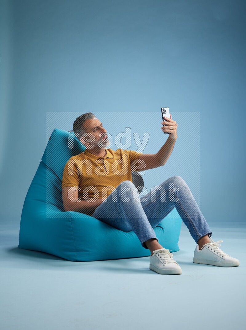 A man sitting on a blue beanbag and taking selfie