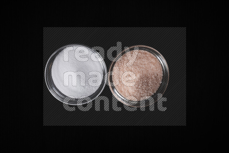 2 glass bowls one is filled with himalayan salt and the other with white salt on black background