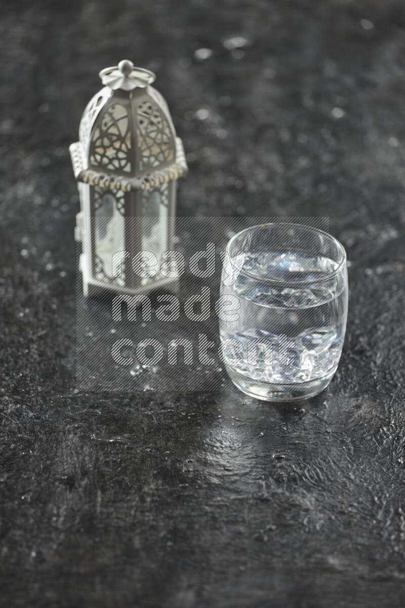A white lantern with different drinks, dates, nuts, prayer beads and quran on textured black background