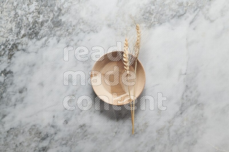 Wheat stalks on multicolored pottery plate on grey marble background
