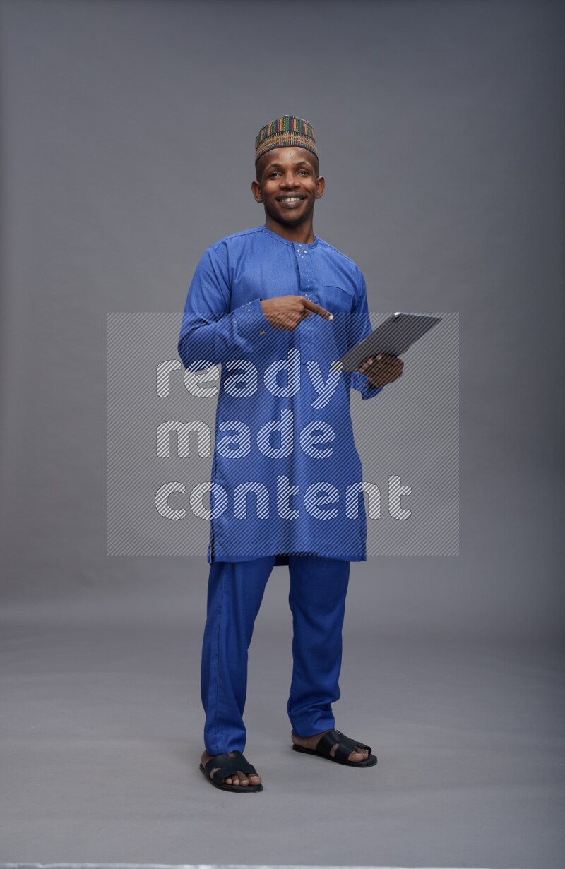 Man wearing Nigerian outfit standing working on tablet on gray background