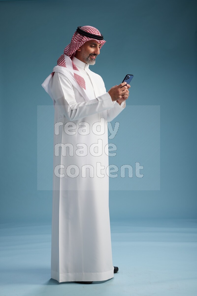 Saudi man wearing thob and shomagh texting on blue background
