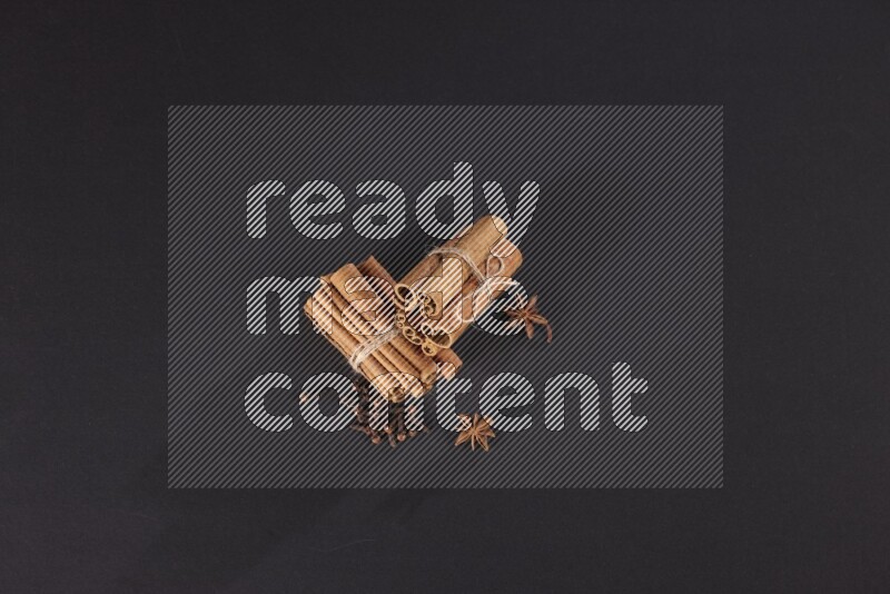 Two bounded stacks of cinnamon sticks with cloves and star anise on black background