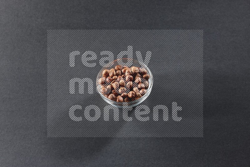 A glass bowl full of peeled hazelnuts on a black background in different angles