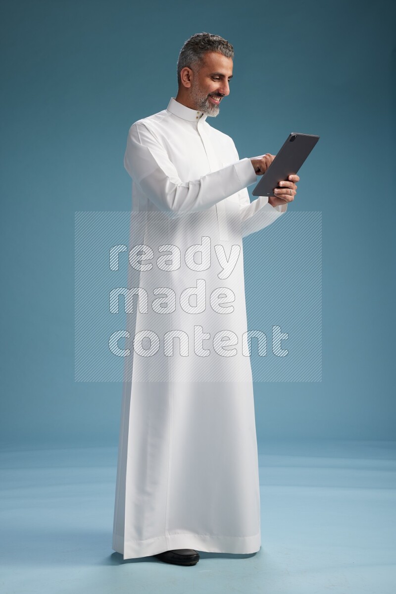 Saudi man waring thob with tablet on blue background