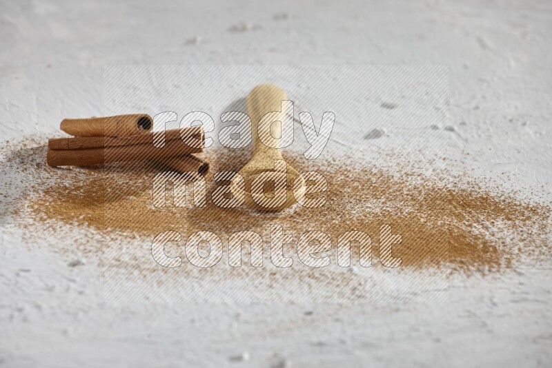 Cinnamon powder in a wooden spoon with cinnamon sticks and sprinkles powder on the flooring on white background