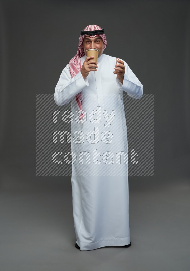 Saudi man with shomag Standing holding paper cup on gray background