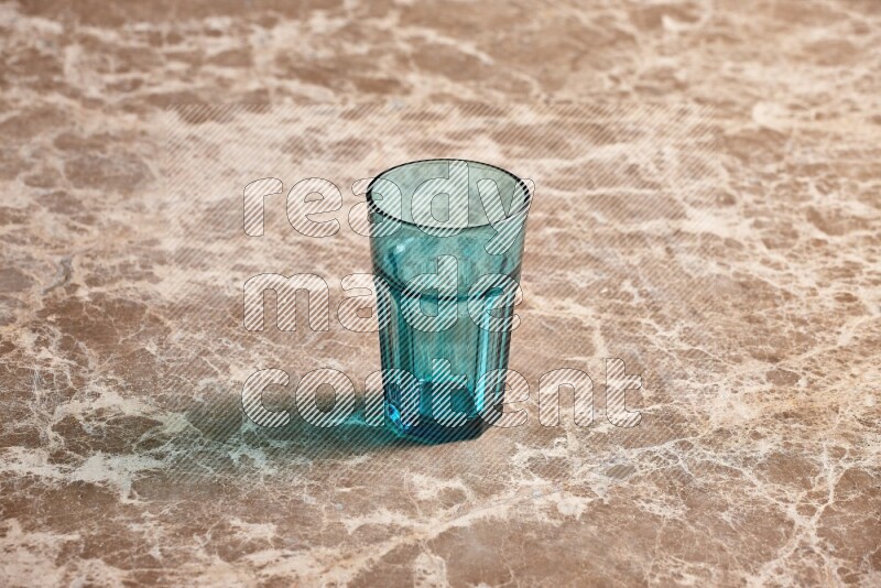 A turquoise glass cup on beige marble background