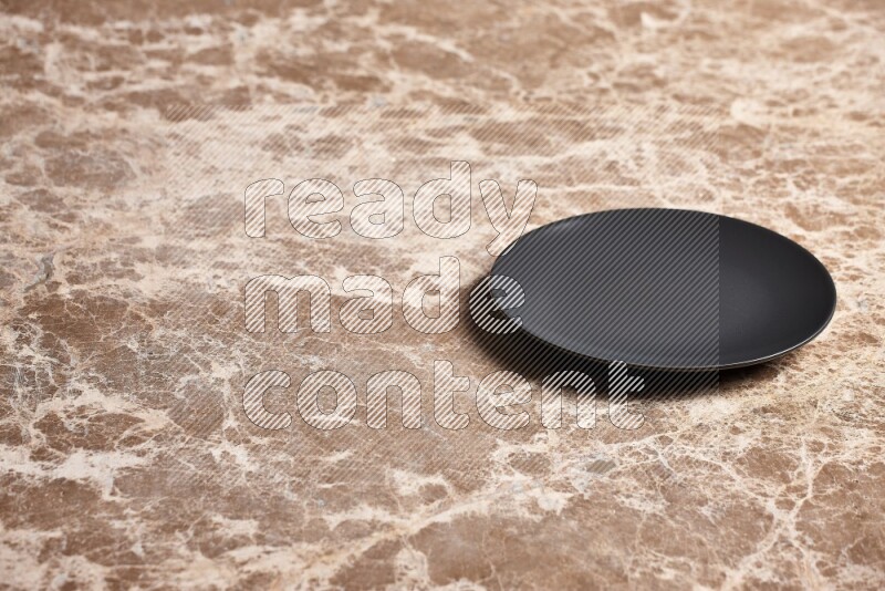A black ceramic circular plate on beige marble background