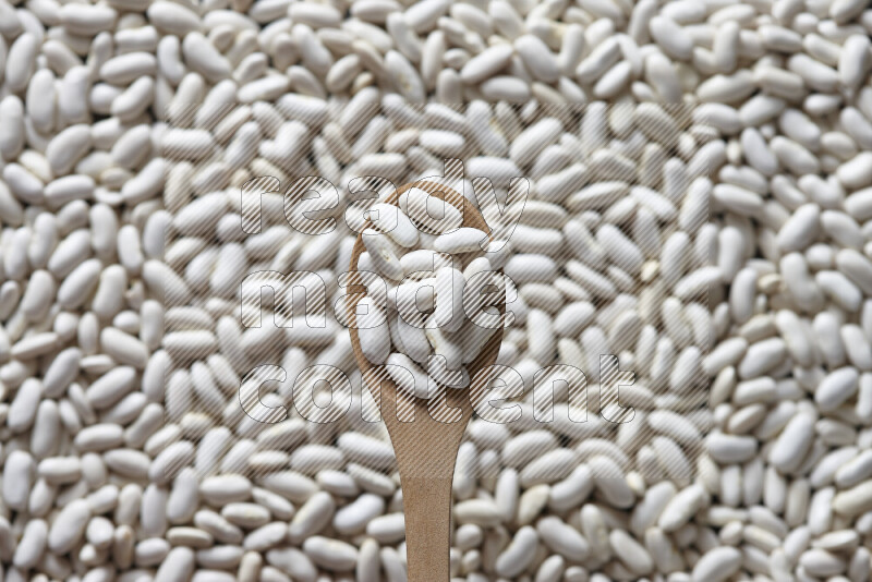 A wooden spoon full of white beans on white beans background