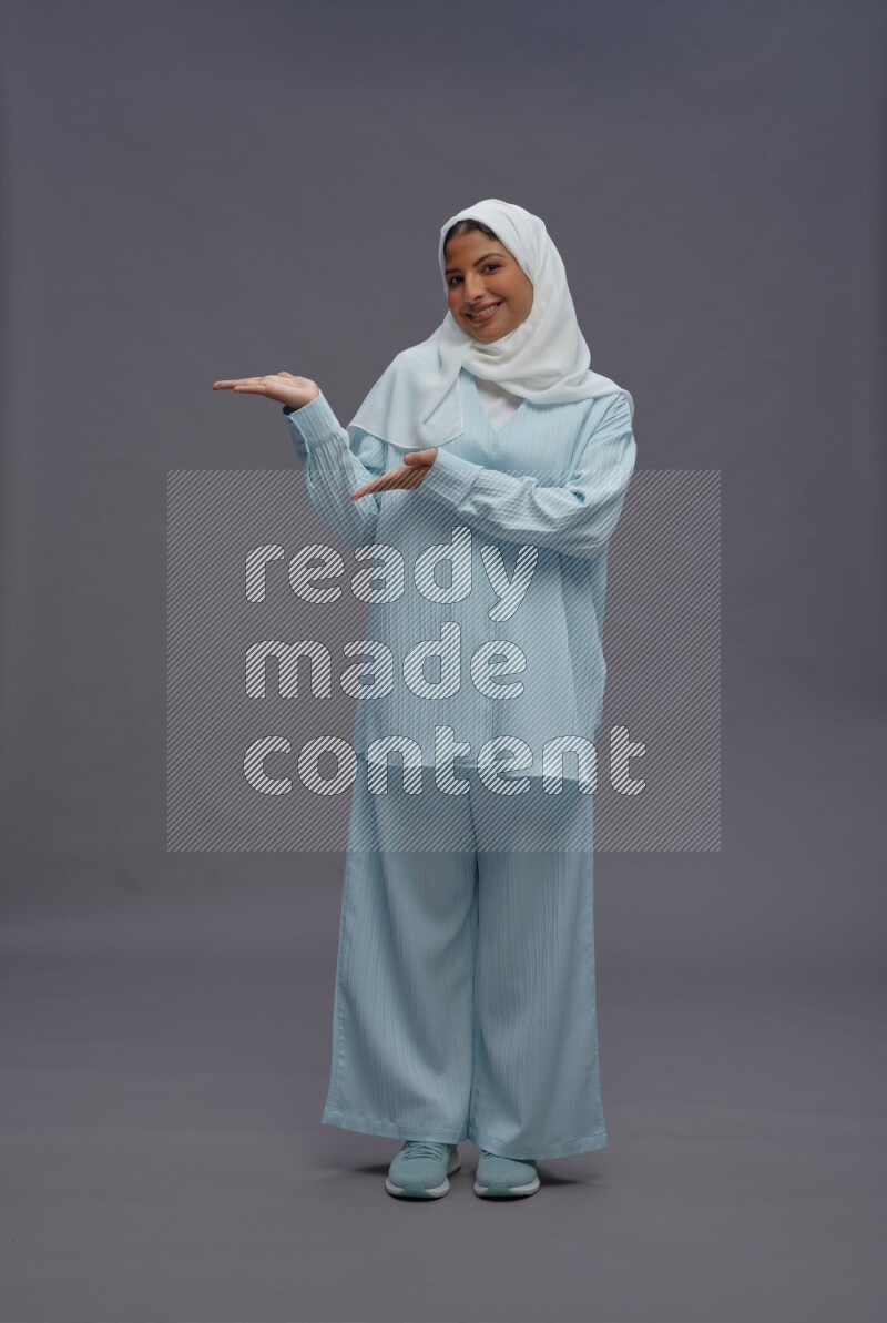Saudi woman wearing hijab clothes standing interacting with the camera on gray background