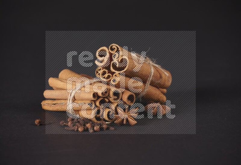 Two bounded stacks of cinnamon sticks with cloves and star anise on black background